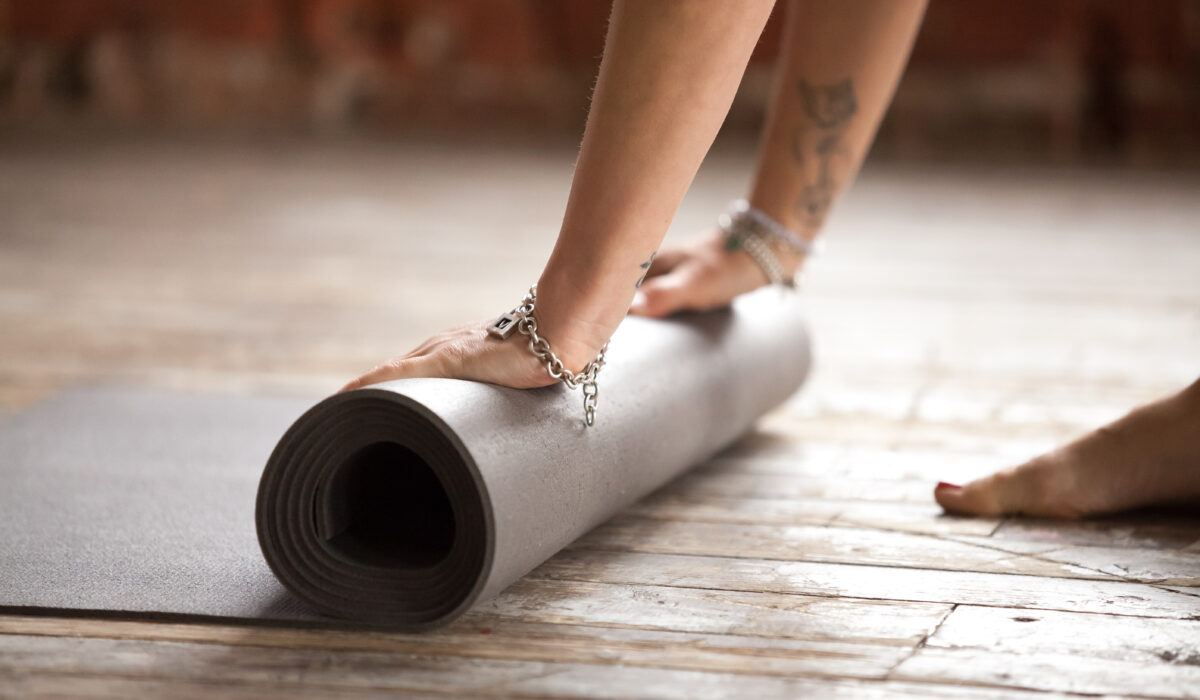 Mains de femme roulant un tapis de yoga sur un parquet en bois brut.