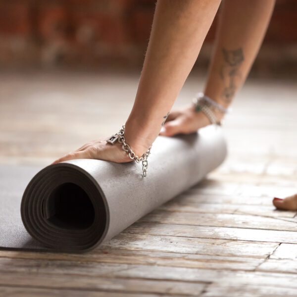 Mains de femme roulant un tapis de yoga sur un parquet en bois brut.