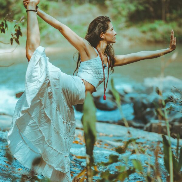 Femme long cheveux détachés en jupe longue blanche exerçant la posture dandayamana , prés d'une rivière dans une forêt